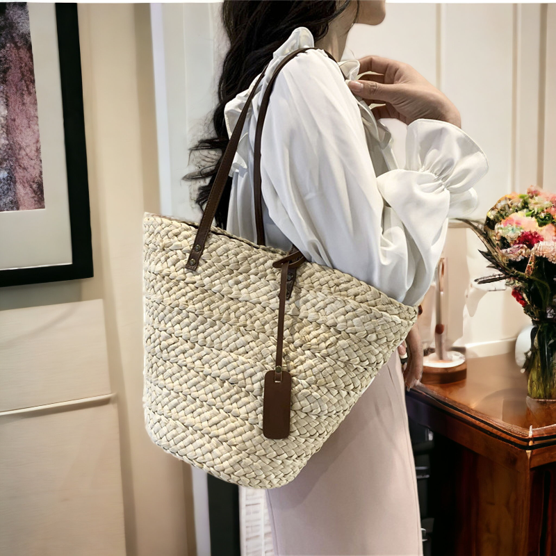 An image of a women showcasing a handwoven straw bag with faux leather straps.